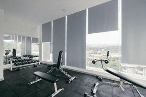 Ein Fitnessstudio mit Trainingsgeräten, großen Fenstern und Blick auf die Stadt.