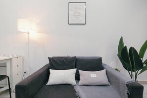 A room with a dark-colored sofa, a desk with a lamp, and a framed quote on the wall.