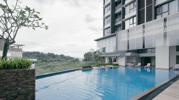 A swimming pool with lounge chairs, a stone planter, and a modern building with balconies. - Mini House Gombak2BR 5paxAyuman Suites (Setapak)