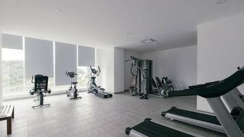A gym with various exercise equipment, large windows, and a tiled floor.