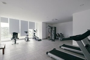A gym with various exercise equipment, large windows, and a tiled floor.