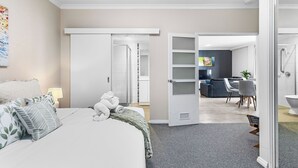 A modern hotel room with a large bed, a desk, and a dining area visible through an open door. - East Perth Escape | WiFi • Parking (East Perth)