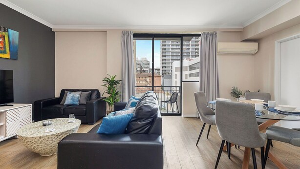 A modern living room with a black leather sofa, a round coffee table, and a dining area with grey chairs and a table. - East Perth Escape | WiFi • Parking (East Perth)