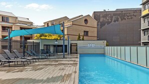 A swimming pool with lounge chairs and a shaded area, surrounded by buildings. - East Perth Escape | WiFi • Parking (East Perth)