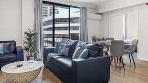 A modern living room with a dark sofa, a round coffee table, and a dining area with chairs and a table. - East Perth Escape | WiFi • Parking (East Perth)