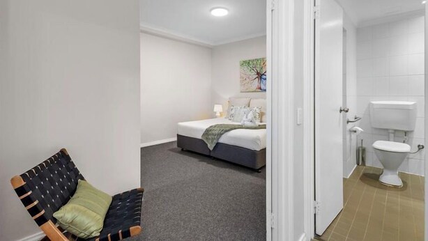 A bedroom with a bed, a chair, and a bathroom visible through an open door. - East Perth Escape | WiFi • Parking (East Perth)