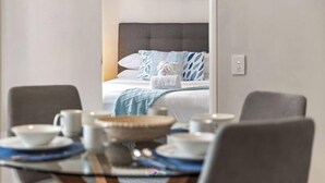A hotel room with a bed, a dining table with plates and cups, and a colorful abstract painting on the wall. - East Perth Escape | WiFi • Parking (East Perth)