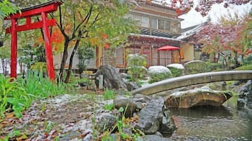 A traditional Japanese garden with a stone bridge, a red torii gate, and a building with a tiled roof.