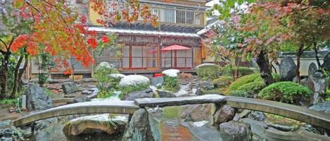Un jardín japonés tradicional con un puente de piedra, un estanque de carpas y un edificio de techo rojo.