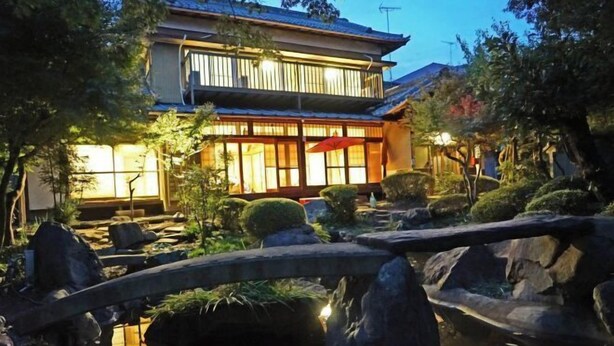 A traditional Japanese-style building with a wooden bridge over a pond, surrounded by rocks and greenery. - Iidaya Hotel (Yokohama)