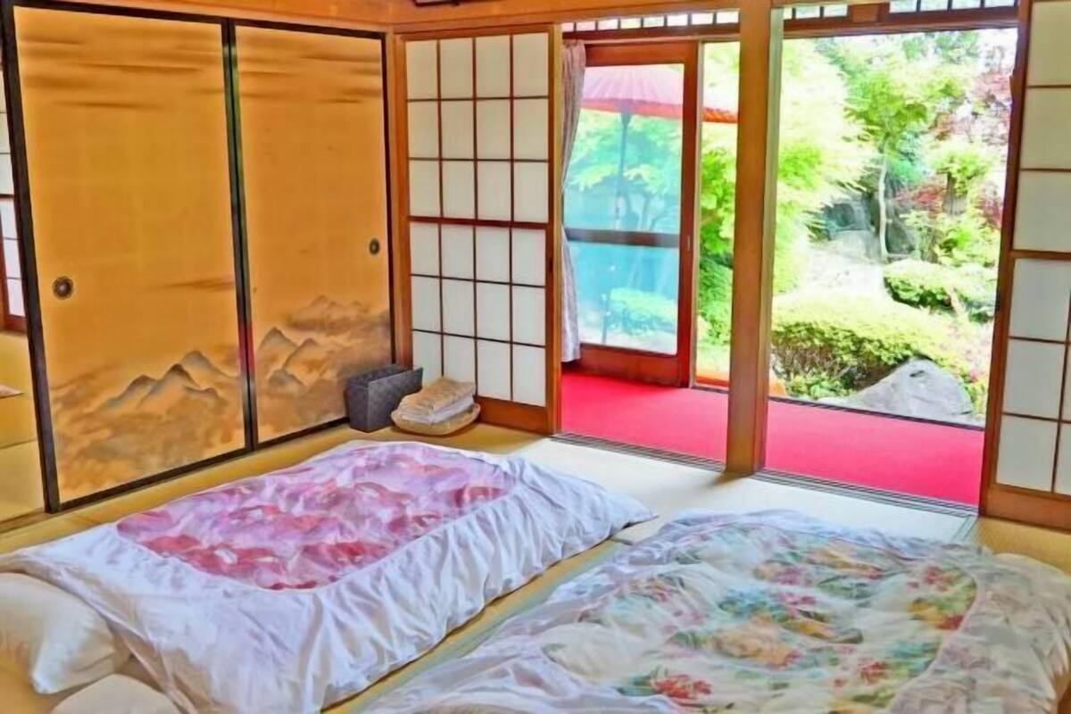 Une pièce de style japonais traditionnel, avec un sol recouvert de tatamis, un lit agrémenté de motifs floraux, des portes coulissantes et une vue sur un jardin.