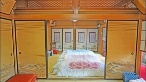 A traditional Japanese room with tatami flooring, a bed with a white and pink bedspread, and sliding doors with mountain designs. - Iidaya Hotel (Yokohama)