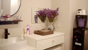 A bathroom with a sink, mirror, vase with flowers, toiletries, and a water dispenser. - MIIYAVI Hotel (Tokyo)