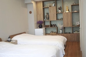 A bedroom with two beds, a wooden cabinet with shelves, and a small refrigerator.
