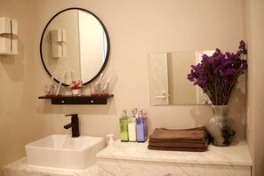 A bathroom with a white sink, a round mirror, a vase with purple flowers, and a towel on the counter. - MIIYAVI　Hotel (Tokyo)