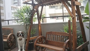 A wooden swing chair, a dog, and potted plants on a balcony with a city view. - MIIYAVI Hotel (Tokyo)