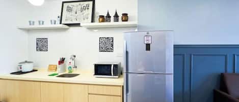 A kitchen with a refrigerator, microwave, and wooden cabinets. There are shelves above the counter with decorative items.