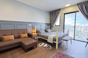 A bedroom with a bed, a sofa, a chair, a nightstand, and a view of the outdoors. - Pool View Air-Con Studio @Tiara Imperio Bangi (Kajang)