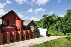 A red building with a balcony, surrounded by greenery and a clear sky. - VILLA ELIZA CANGGU (Bali)