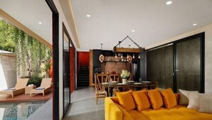 A modern living room with a yellow sofa, a dining area with a brick wall, and a poolside area with lounge chairs. - VILLA ELIZA CANGGU (Bali)