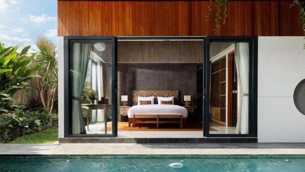 A modern bedroom with a large bed, a nightstand, and a window overlooking a swimming pool. - VILLA ELIZA CANGGU (Bali)