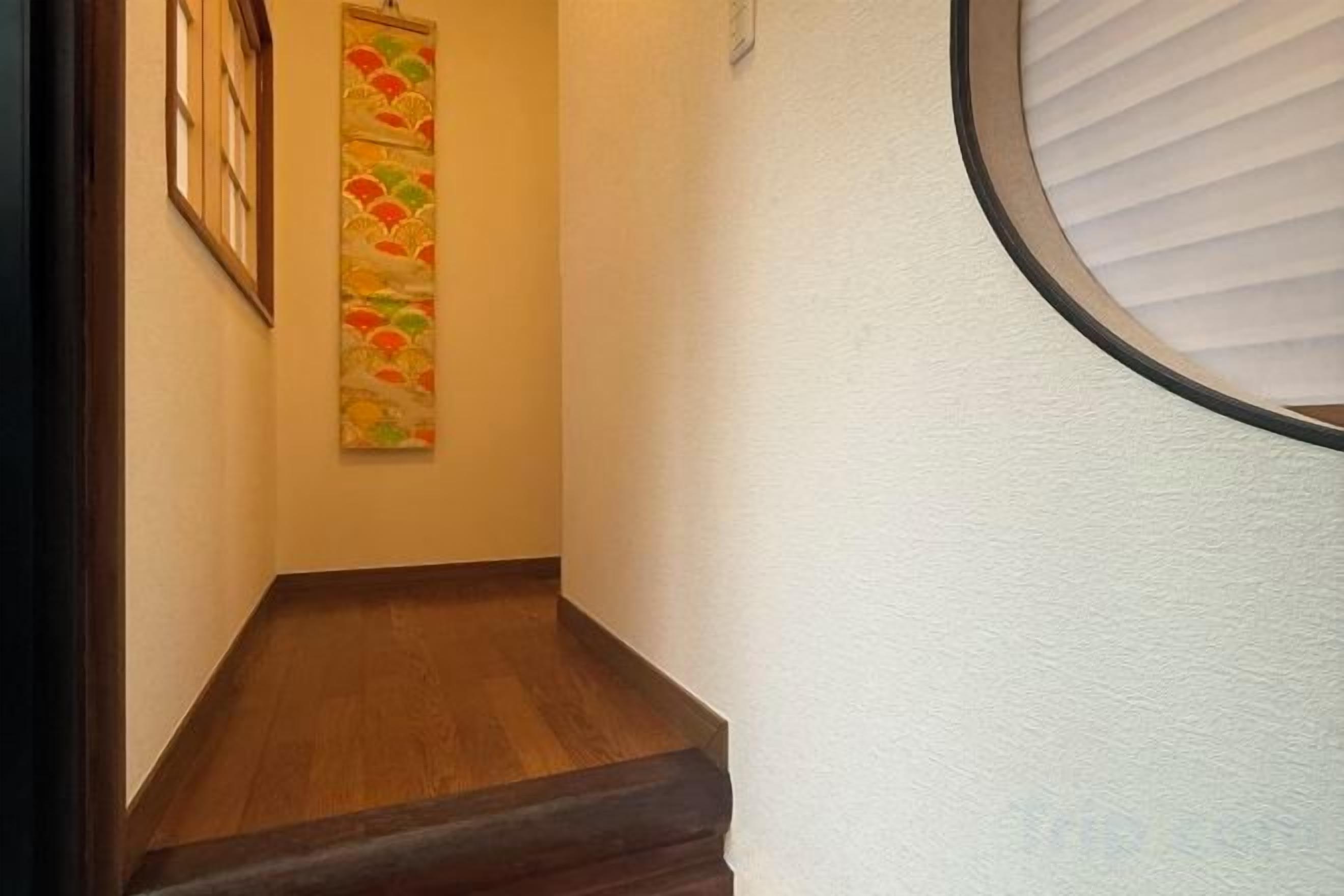 Un pasillo estrecho con piso de madera, una obra de arte en la pared y una ventana con persianas.