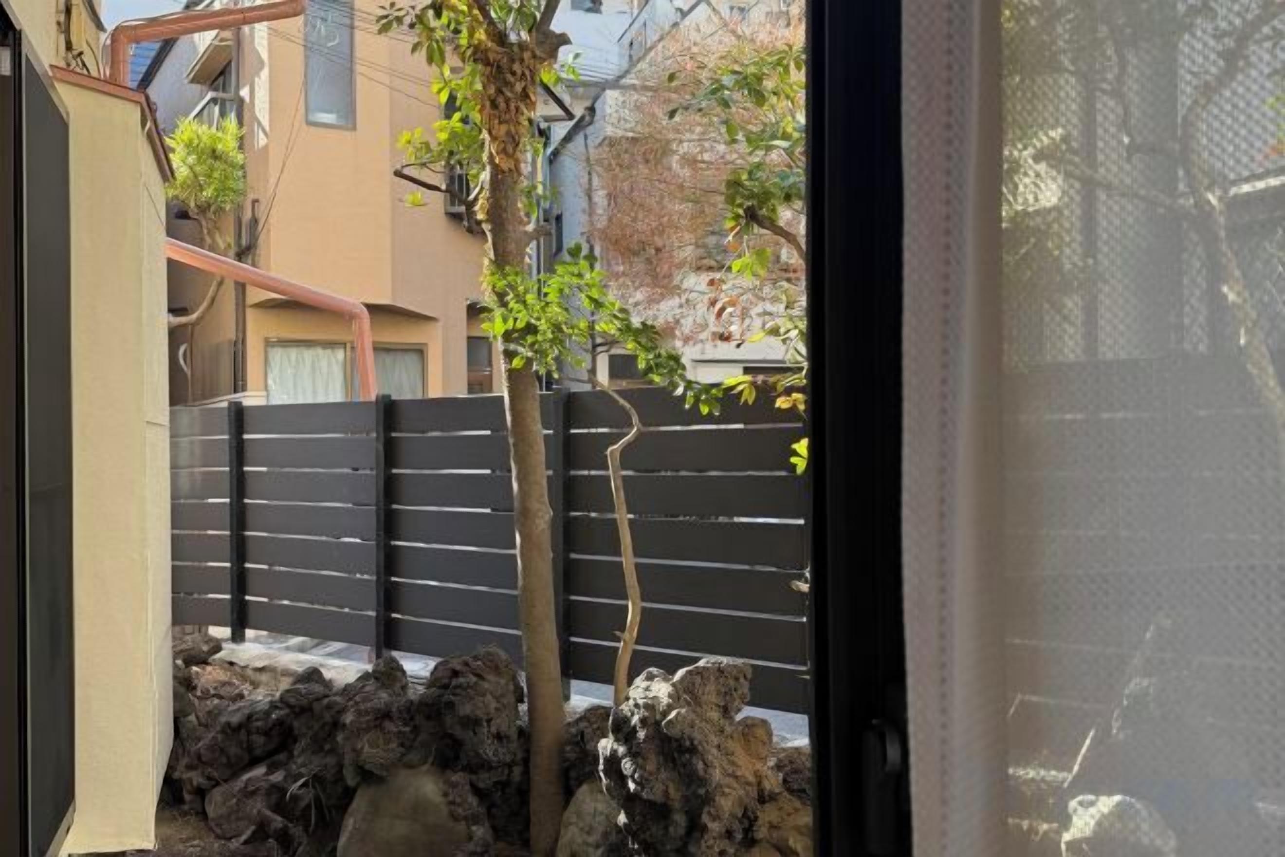 Vista de un patio con valla negra, un árbol y un muro de piedra.
