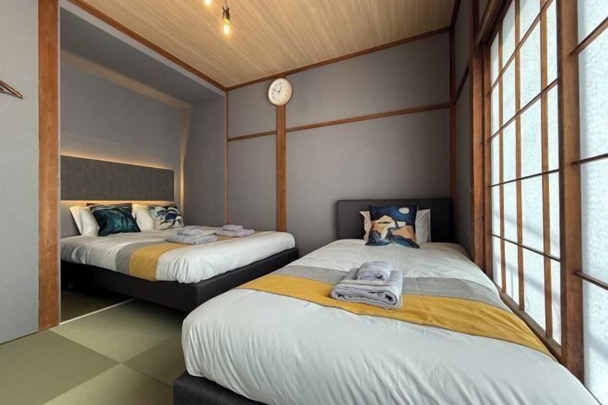 A hotel room with two beds, a clock, and large windows.