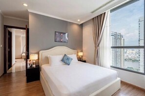 Una habitación de hotel moderna con una cama grande, una mesita de noche, una lámpara, un cuadro en la pared y vistas de la ciudad a través de la ventana.
