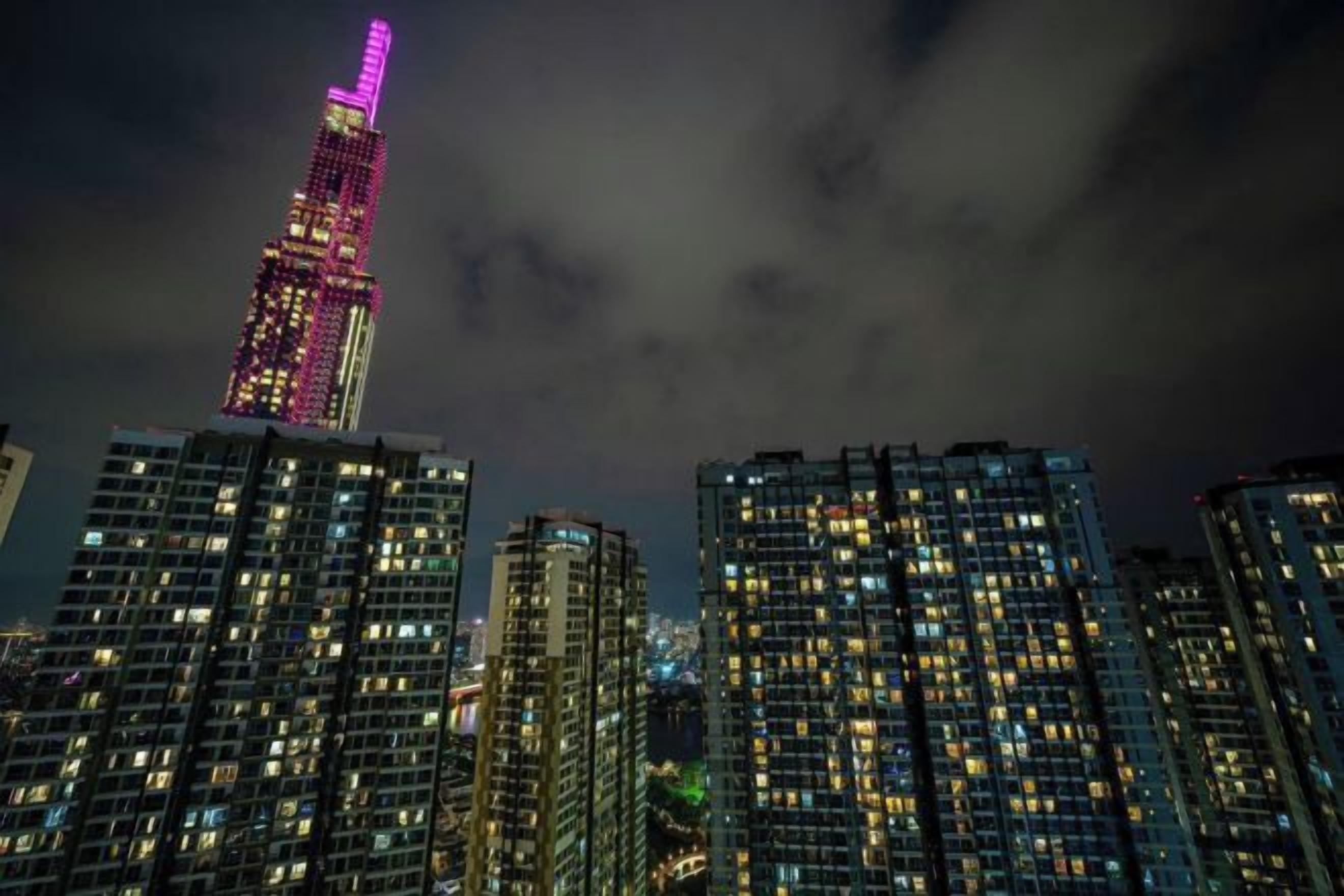 Ein nächtliches Stadtbild mit beleuchteten Wolkenkratzern und einem markanten Gebäude in pinkfarbenem Licht.