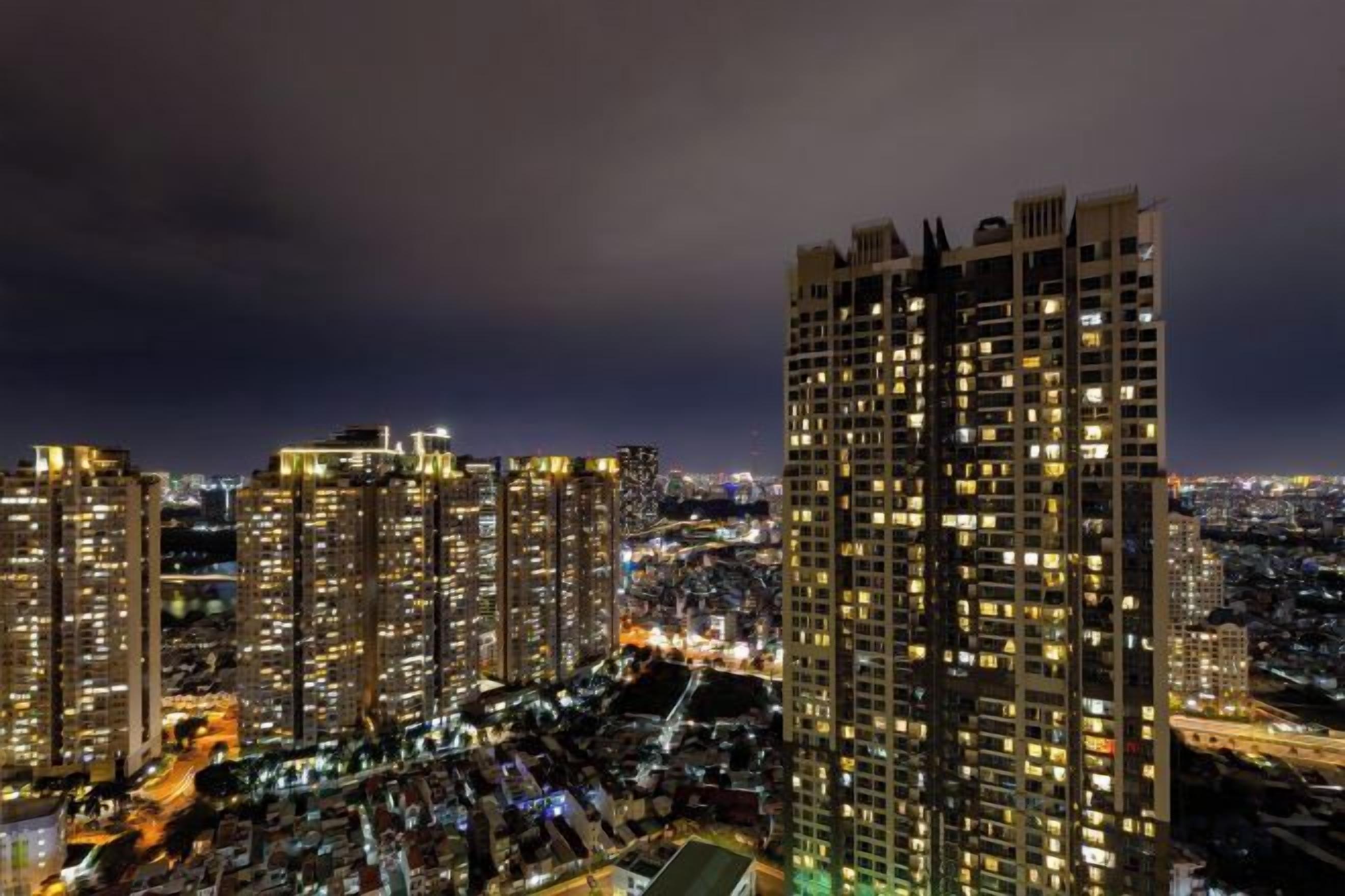 A high-rise building with multiple floors and numerous windows, surrounded by a cityscape at night.