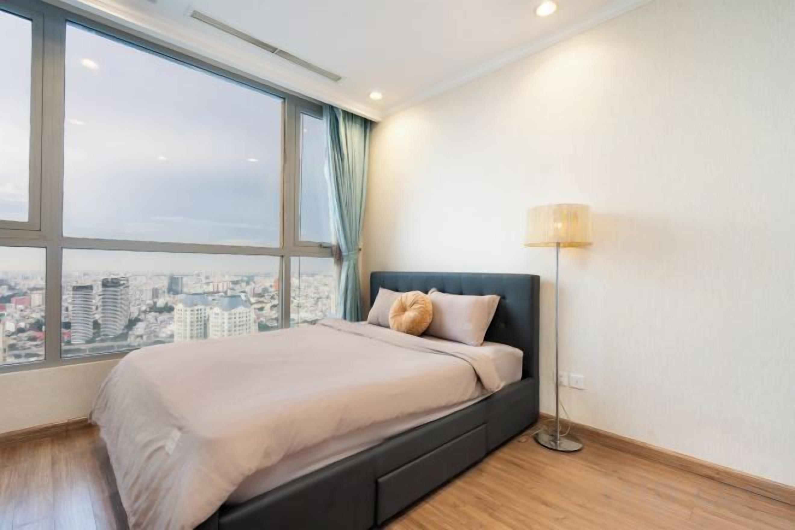 A bedroom with a bed, a window with a view of a cityscape, and a floor lamp.