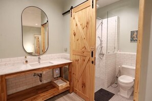 Een badkamer met een houten deur, witte tegels, een wastafel en een toilet.