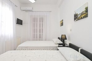Une chambre d’hôtel avec deux lits, un téléviseur à écran plat, une table de chevet avec une lampe et une fenêtre avec des rideaux légers.