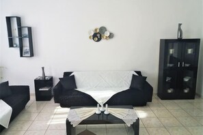 Un salon avec un canapé noir, une table basse recouverte d’une nappe blanche, un meuble et des éléments de décoration murale.