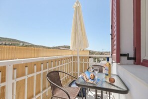 A balcony with wicker chairs, a table, a yellow umbrella, and a bottle of wine. - Akakia Residence (Naxos)