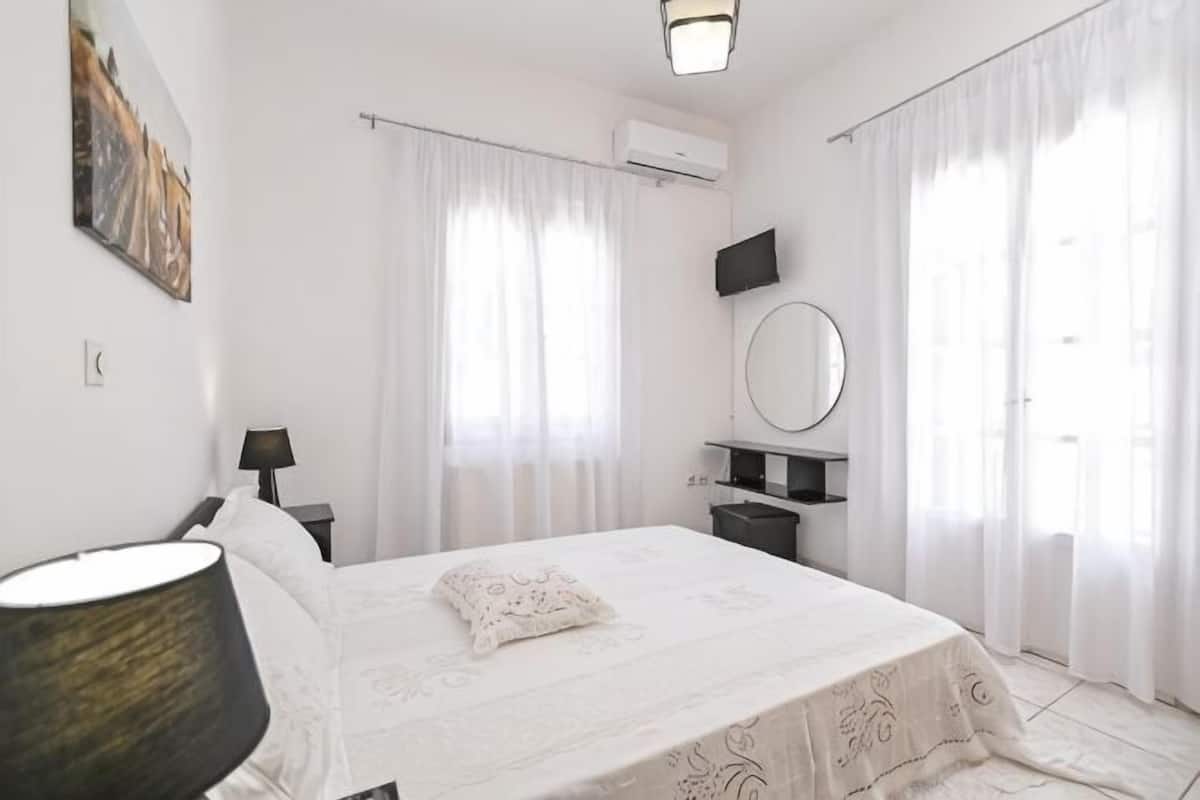 A bedroom with a bed, bedside tables, a lamp, a mirror, and curtains.