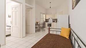A bedroom with a bed, a bedside table, a window, and a view of the kitchen. - Akakia Residence (Naxos)