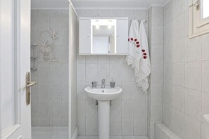 A bathroom with a white sink, a mirror above it, and a shower area. - Akakia Residence (Naxos)
