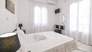 A bedroom with a bed, a bedside table, a lamp, a mirror, and a window with curtains. - Akakia Residence (Naxos)