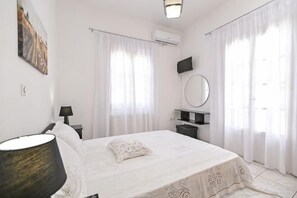 Una camera da letto con un letto, un comodino, una lampada, uno specchio e una finestra con tende.