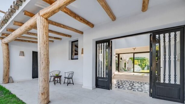 Ein überdachter Außenbereich mit einer Pergola, zwei Stühlen und einer zur Garten führenden Tür.