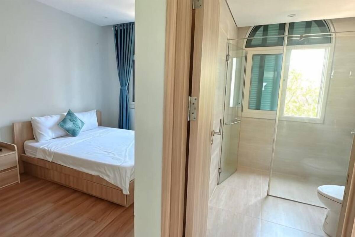 A bedroom with a bed, bedside table, and a shower area with a glass door.