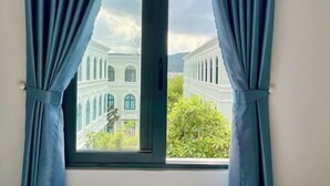 A window with curtains, offering a view of a building with arched windows and a white facade. - Nhà Nguyên Căn Costis 5 Phòng Ngủ (Phu Quoc Island)