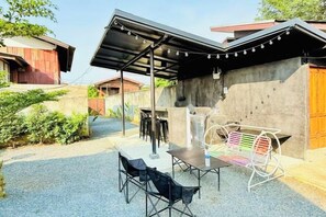 An outdoor patio with a table and chairs, a covered seating area, and string lights. - Cina Home (Chiang Mai)