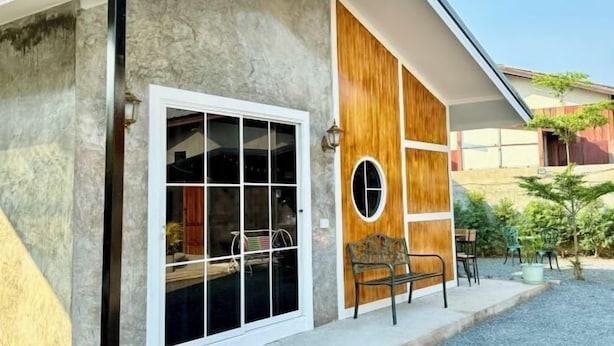 A modern building with a large glass door, a wooden panel wall, and a small outdoor seating area with a bench and chairs. - Cina Home (Chiang Mai)