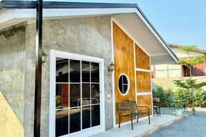 A modern building with a large glass door, a wooden panel wall, and a small outdoor seating area with a bench and chairs. - Cina Home (Chiang Mai)