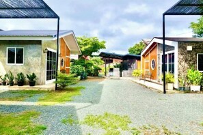 A courtyard with buildings, gravel path, and potted plants. - Cina Home (Chiang Mai)