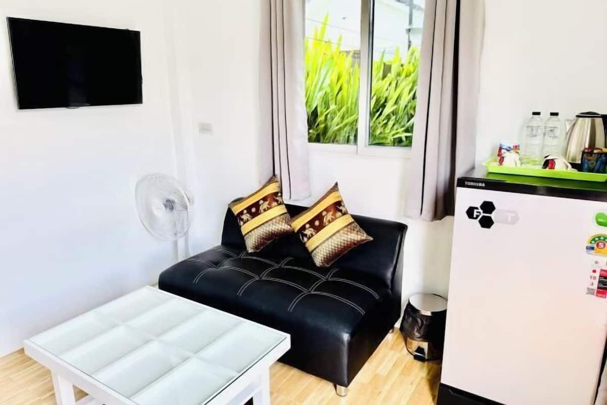 A compact living space with a sofa, a small table, a refrigerator, and a window with curtains.