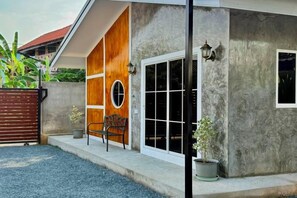 A house with a concrete exterior, a wooden door, a window, and a potted plant. - Cina Home (Chiang Mai)